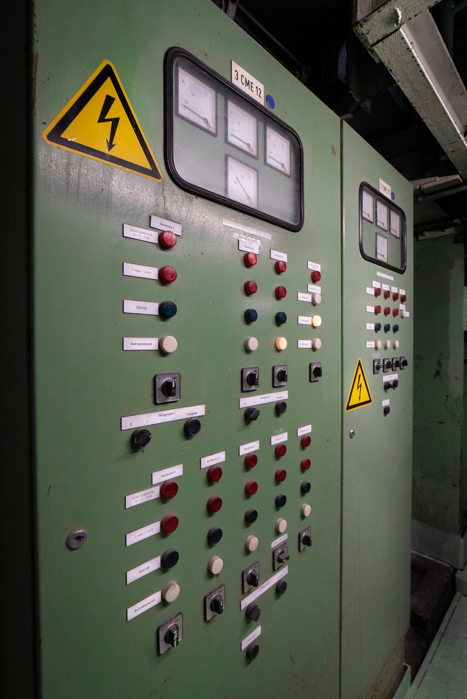 Pannello di controllo industriale verde usurato con molte luci e interruttori.