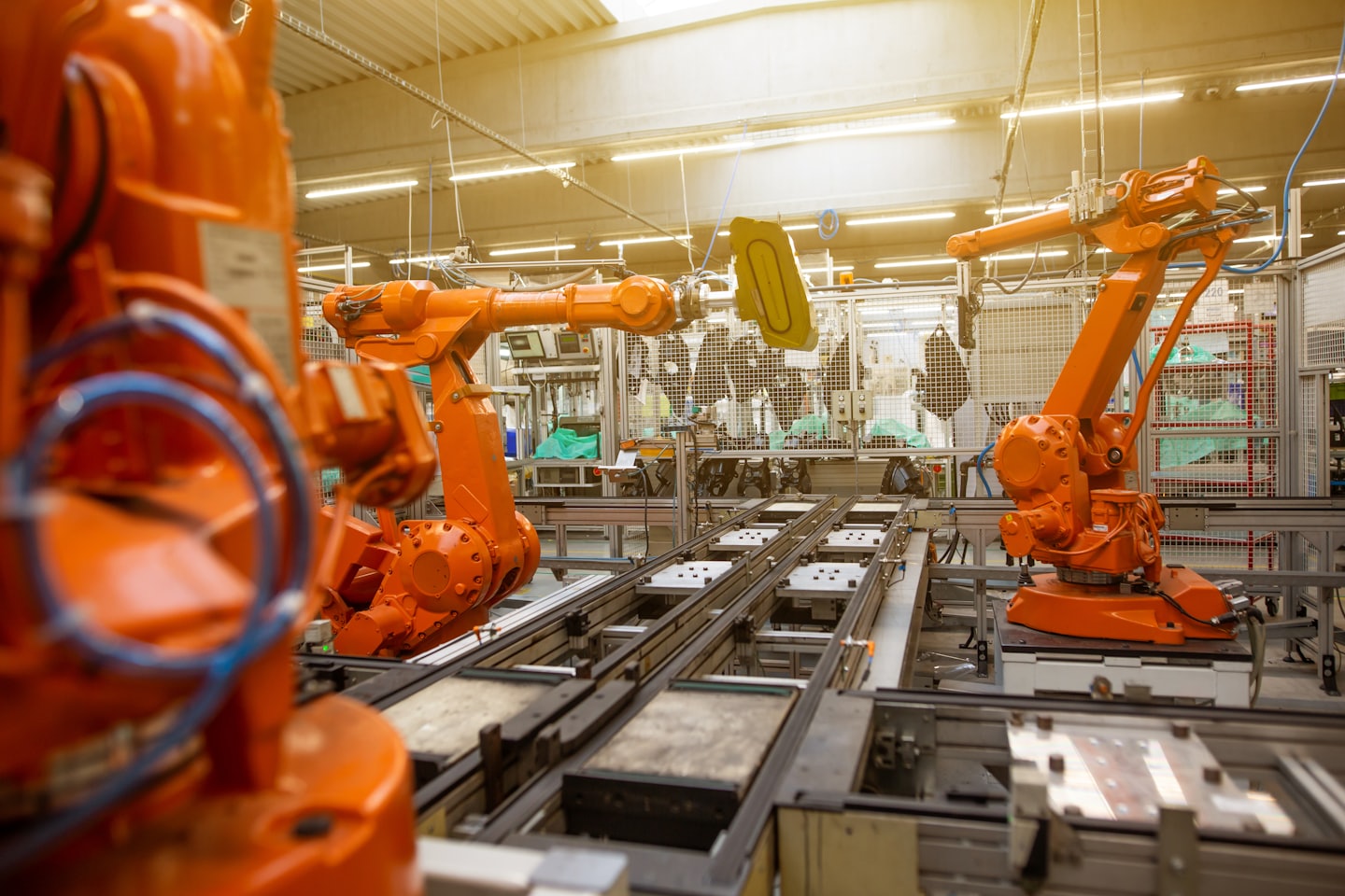 Bracci robotici assemblano componenti su un pavimento di fabbrica ben illuminato.